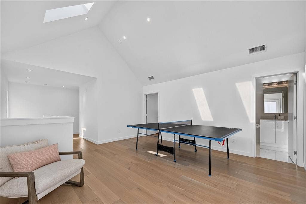 Vaulted ceiling with skylight, recessed lighting, and wood-finish flooring