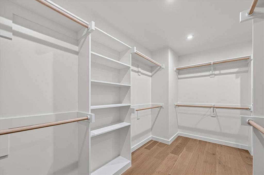 Walk-in closet featuring built-in shelving, multiple hanging rods, recessed lighting, and wood-finish flooring