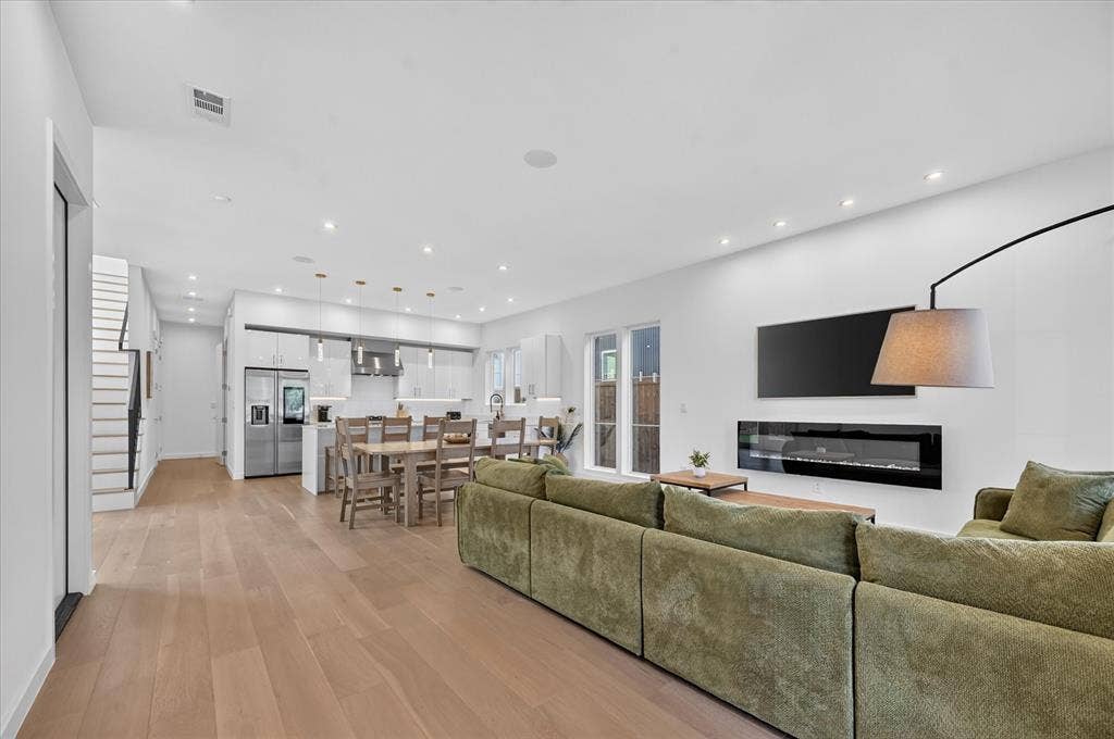 Wood-finish flooring throughout, featuring a modern built-in fireplace, recessed lighting, and a contemporary kitchen with stainless steel appliances