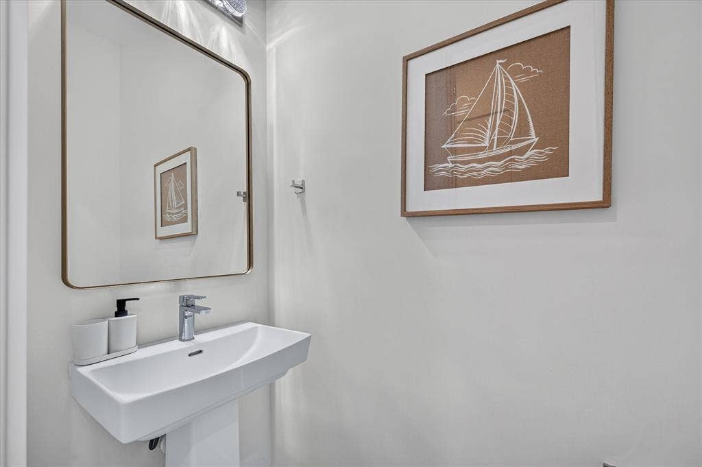 Pedestal sink with a chrome faucet, illuminated by a multi-bulb vanity light, and a framed mirror