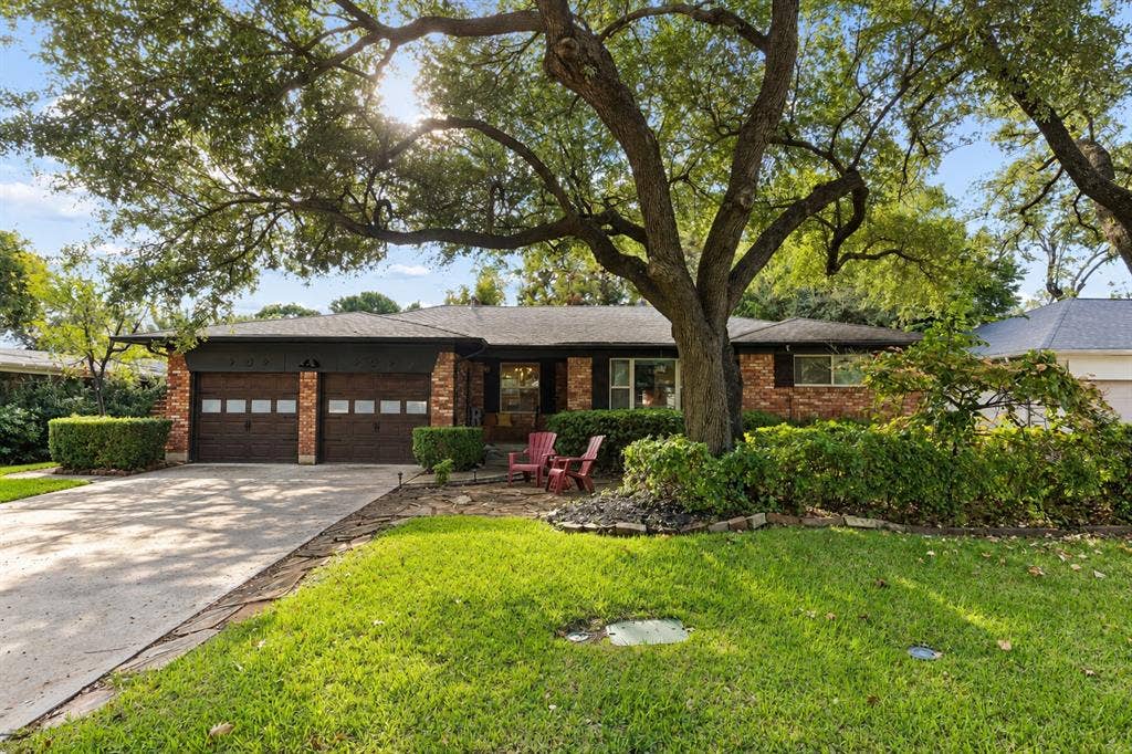 7230 Edgerton Drive, Dallas, TX 75231 Brick exterior residence featuring a two-car garage with glass-panel doors, stone-paved walkway, concrete driveway, and mature canopy trees