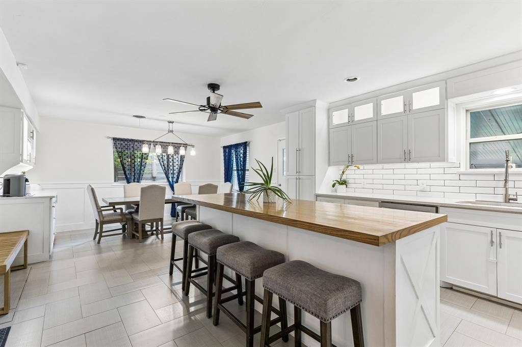 7230 Edgerton Drive, Dallas, TX 75231 Kitchen featuring white shaker-style cabinetry with upper transom glass doors, wood-finish island countertop, white subway tile backsplash, and ceramic tile flooring