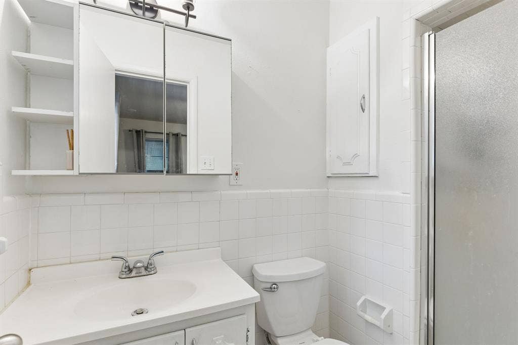 7230 Edgerton Drive, Dallas, TX 75231 Bathroom featuring white wall tiling, a vanity with an integrated sink, a mirrored medicine cabinet with open shelving, and a glass-enclosed shower stall