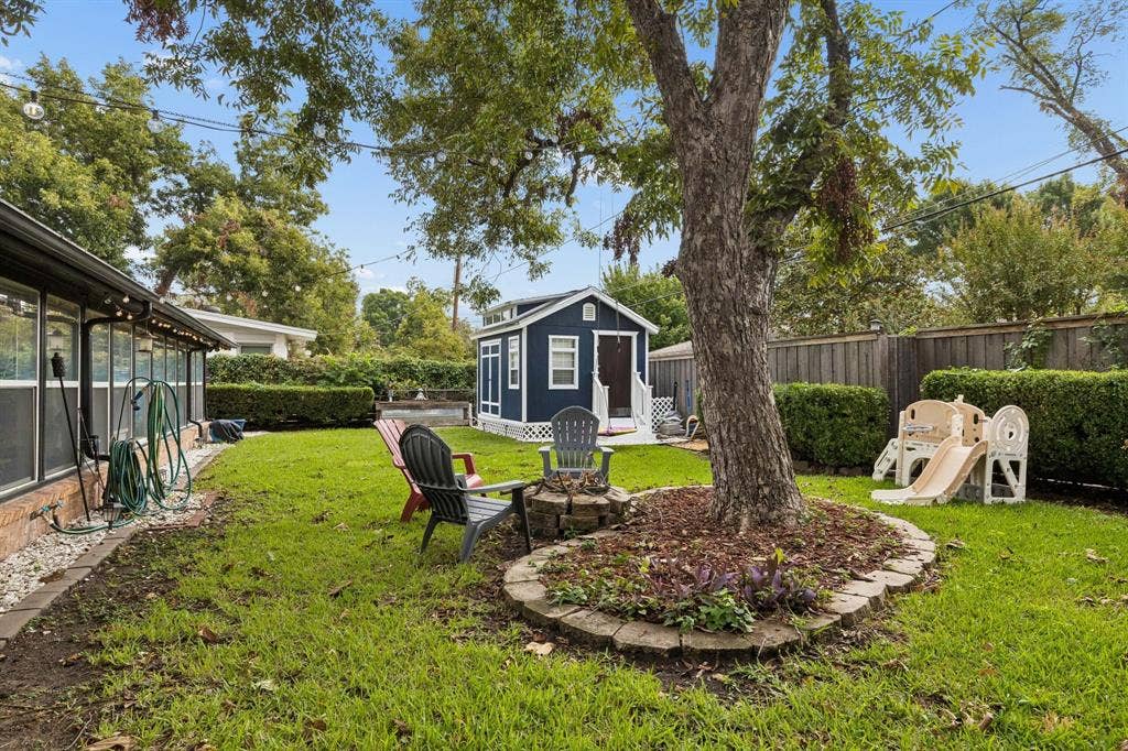 7230 Edgerton Drive, Dallas, TX 75231 Backyard featuring a detached accessory structure, stone-bordered landscaping, mature shade tree, and wood-slat perimeter fencing