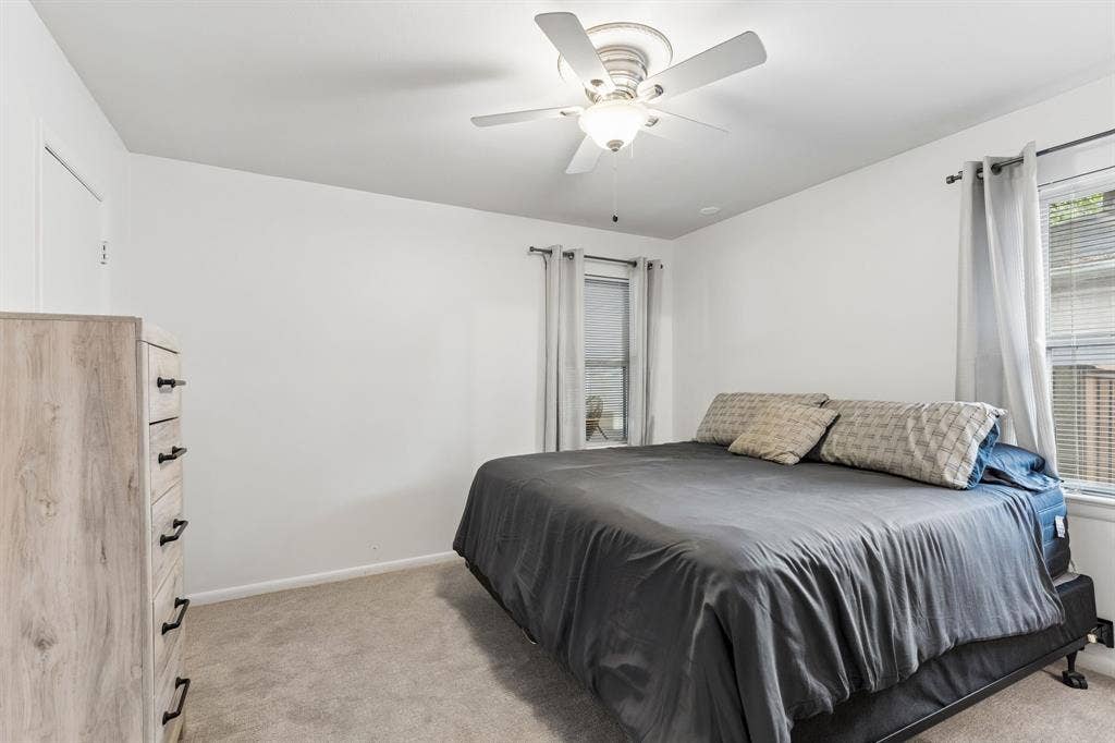 7230 Edgerton Drive, Dallas, TX 75231 Neutral interior featuring carpeting, bright white walls, two windows with adjustable blinds, and a white ceiling-mounted fan with integrated lighting