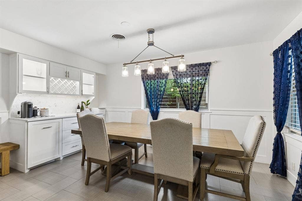 7230 Edgerton Drive, Dallas, TX 75231 Dining area featuring white cabinetry with built-in wine storage, stone-finish countertops, ceramic tile flooring, wainscoting, and a linear pendant light fixture