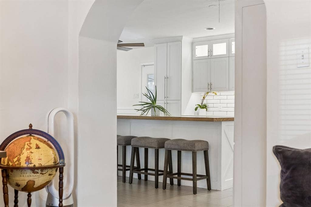 7230 Edgerton Drive, Dallas, TX 75231 Arched entryway featuring white cabinetry, subway tile backsplash, and a breakfast bar with a wooden countertop