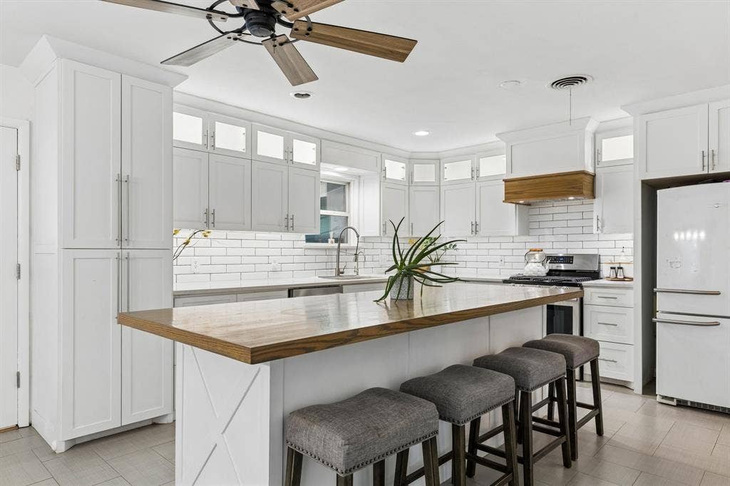 7230 Edgerton Drive, Dallas, TX 75231 Kitchen featuring white shaker cabinetry, a wood-topped island, white subway tile backsplash, crown molding, and a wood-accented range hood