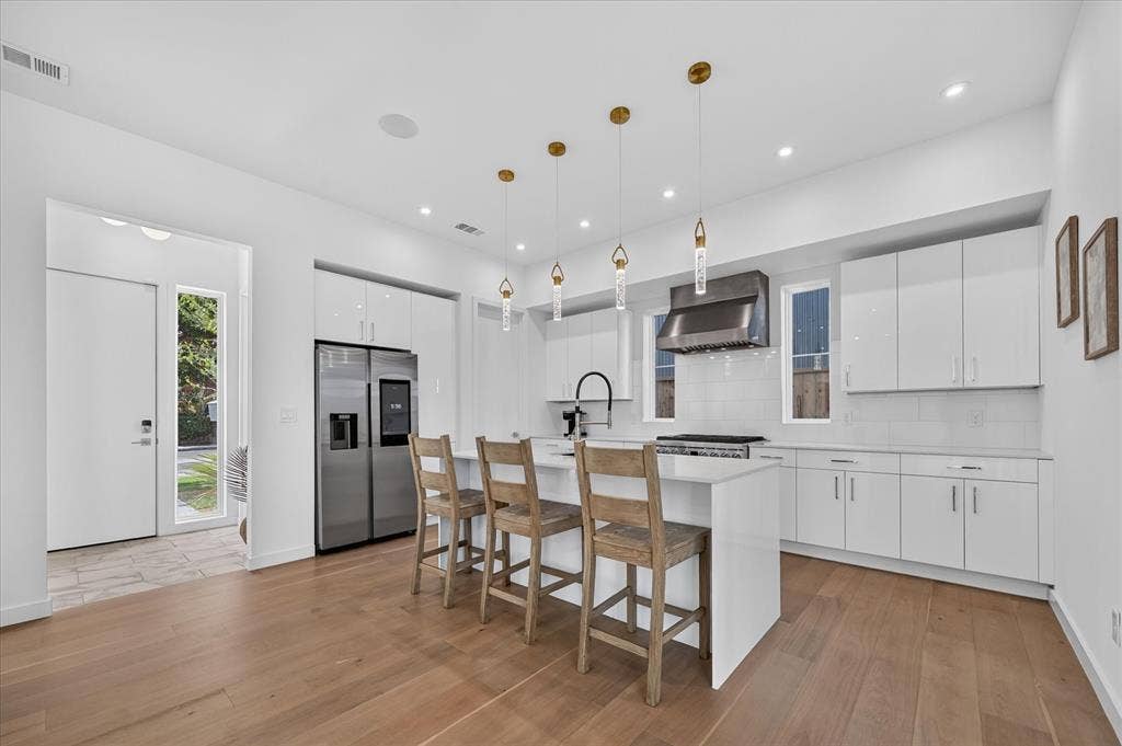 835 Nomas Street, Dallas, TX 75212 Open-concept kitchen with wood-finish flooring, white cabinetry, stainless steel appliances, and an island with pendant lighting