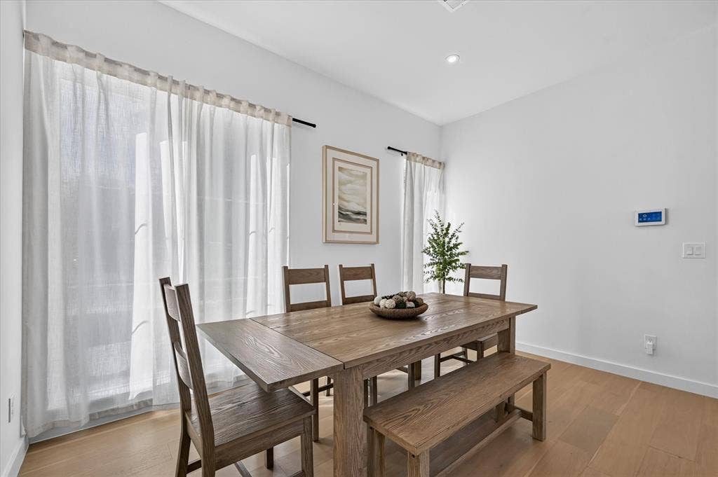 835 Nomas Street, Dallas, TX 75212 Bright dining area showcasing wood-finish flooring, a substantial wood dining table with seating for six, and large windows with sheer curtains providing natural light