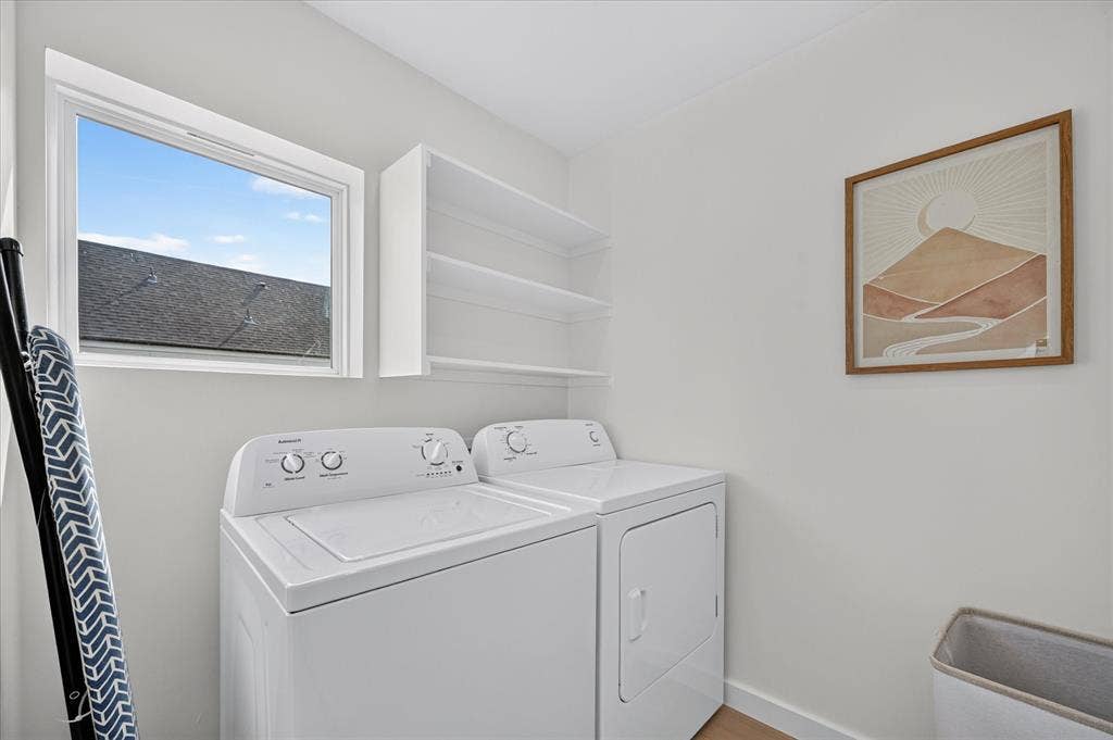835 Nomas Street, Dallas, TX 75212 Dedicated laundry room featuring side-by-side washer and dryer with control-top design, white cabinetry with open shelving for storage, wood-finish flooring, and a transom window providing natural light