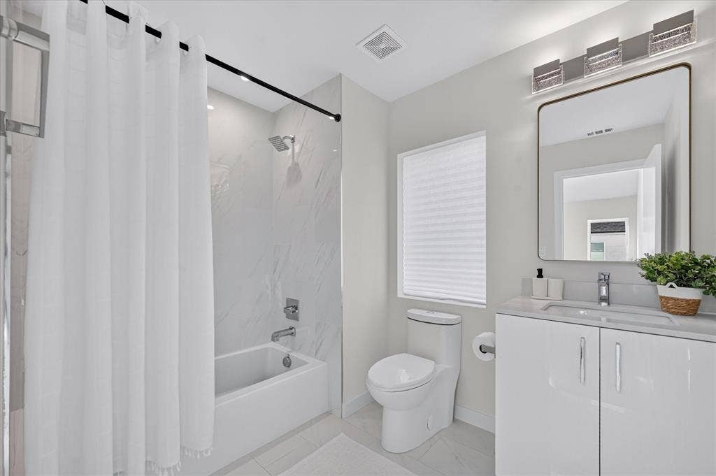 835 Nomas Street, Dallas, TX 75212 Modern bathroom featuring a floating double-vanity with white cabinetry and integrated sink, quartz countertop, framed mirror with integrated lighting, white subway tile flooring, and a separate soaking tub with glass-enclosed shower surround and chrome fixtures