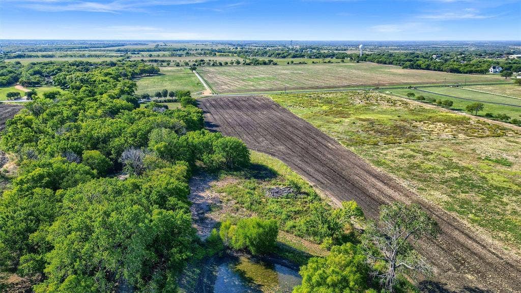 Expansive land parcel featuring natural tree lines, a cultivated field, and a small pond