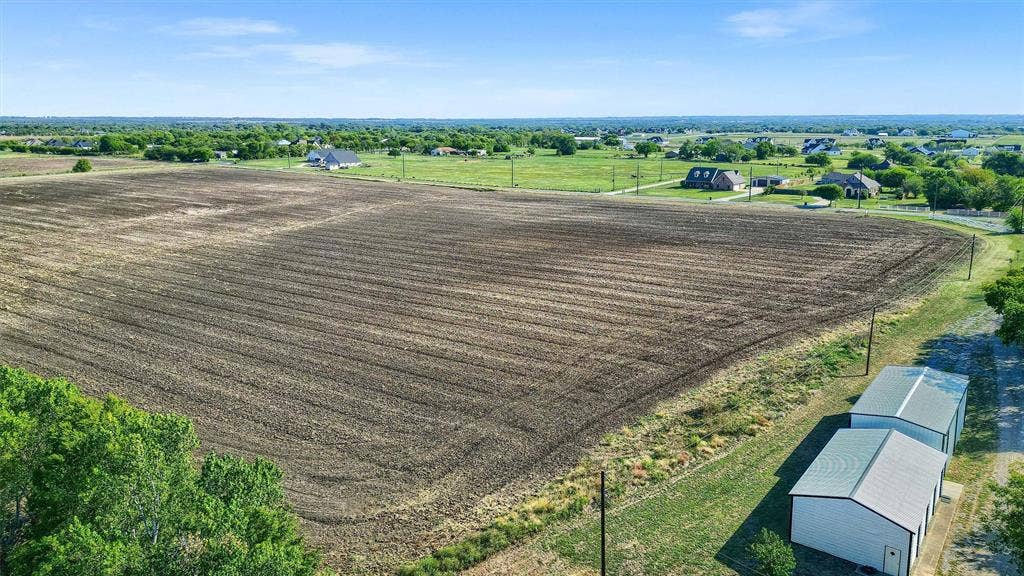Expansive cultivated land parcel with two visible outbuildings featuring metal roofs