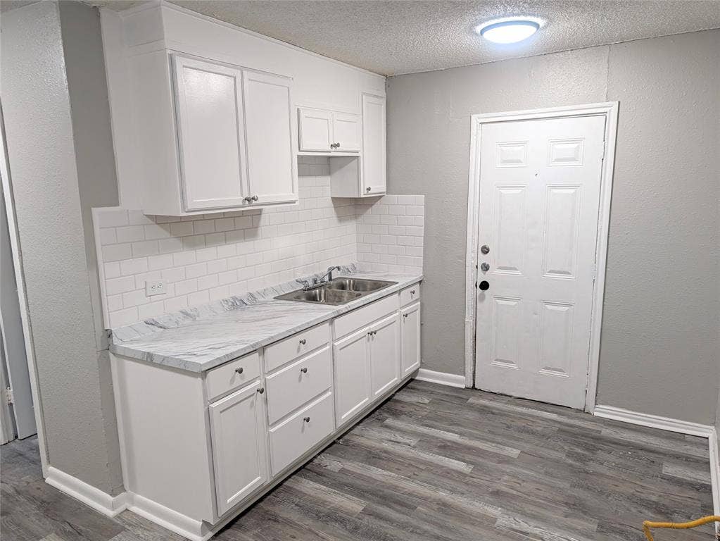 3409 Wood Avenue, Waco, TX 76711 White cabinetry with brushed nickel hardware, white subway tile backsplash, light-toned countertop, double basin stainless steel sink, and wood-finish flooring