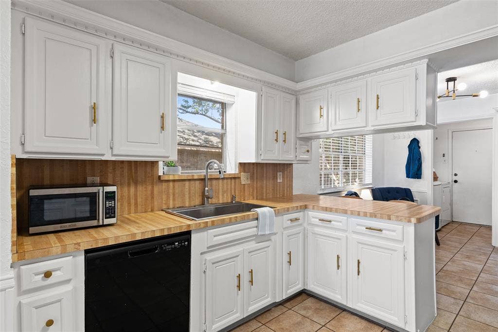 841 Villa Ridge Drive, Garland, TX 75043 White cabinetry with gold-finish hardware, wood-finish countertops, stainless steel sink with a chrome faucet, and integrated black dishwasher