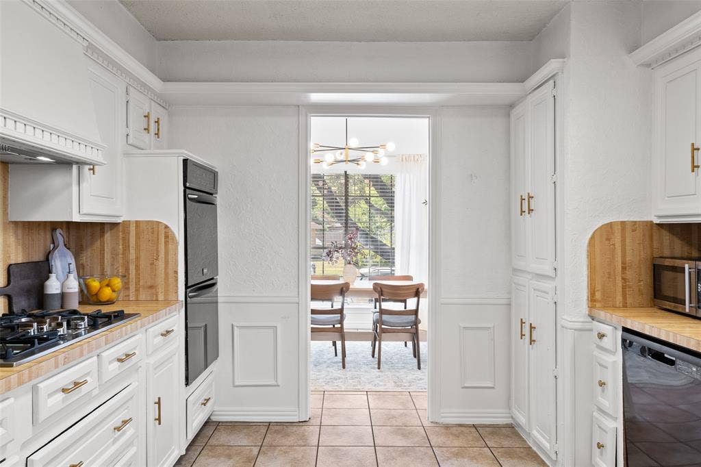 841 Villa Ridge Drive, Garland, TX 75043 White cabinetry with gold-finish hardware, wood-finish countertops, tiled flooring, wainscoting details, and a built-in oven