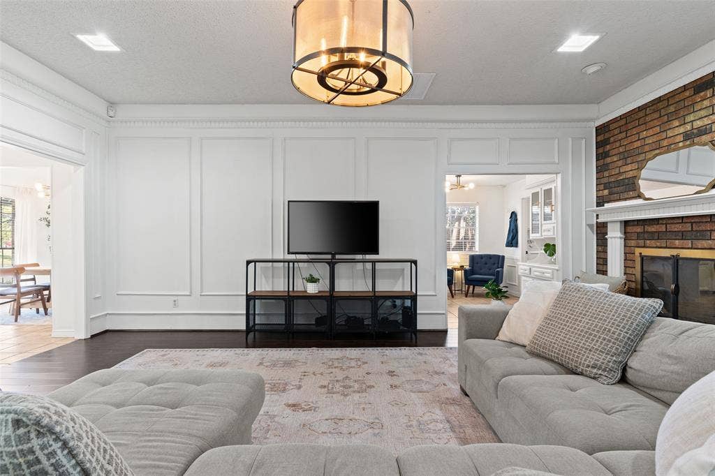841 Villa Ridge Drive, Garland, TX 75043 Hardwood flooring, decorative wall paneling, recessed lighting, brick fireplace with a white mantel, and a prominent ceiling light fixture