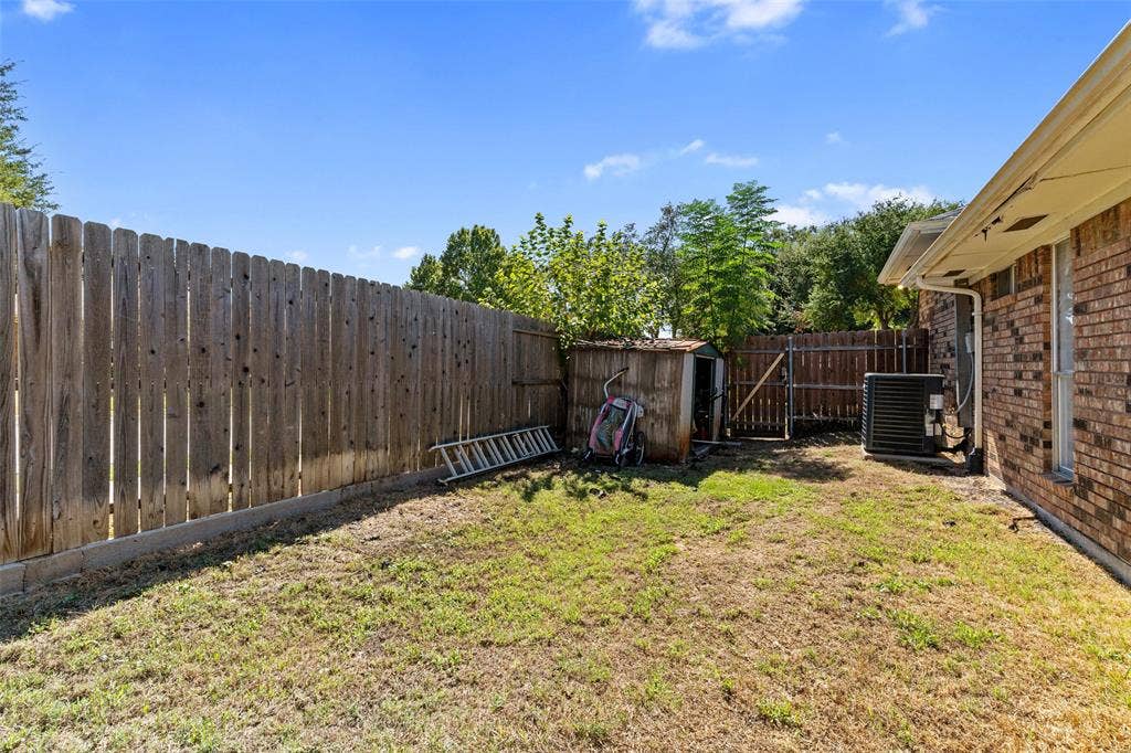 841 Villa Ridge Drive, Garland, TX 75043 Expansive backyard featuring a wood fence, a small storage shed, and a brick exterior wall