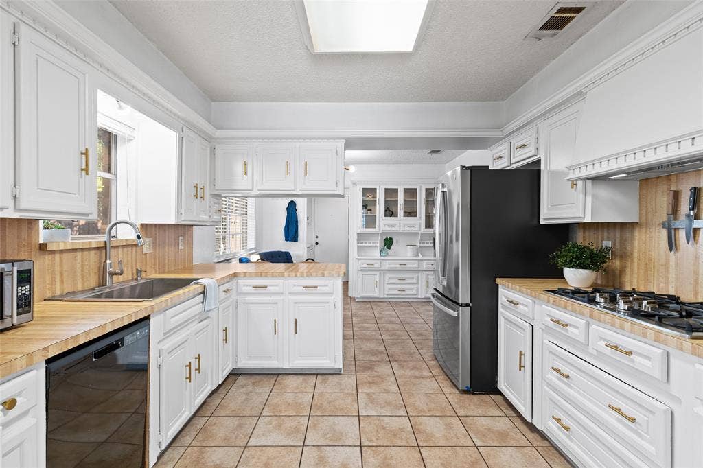 841 Villa Ridge Drive, Garland, TX 75043 White cabinetry with gold-tone hardware, wood-finish countertops, tiled flooring, stainless steel appliances, and a built-in range with a ventilation hood