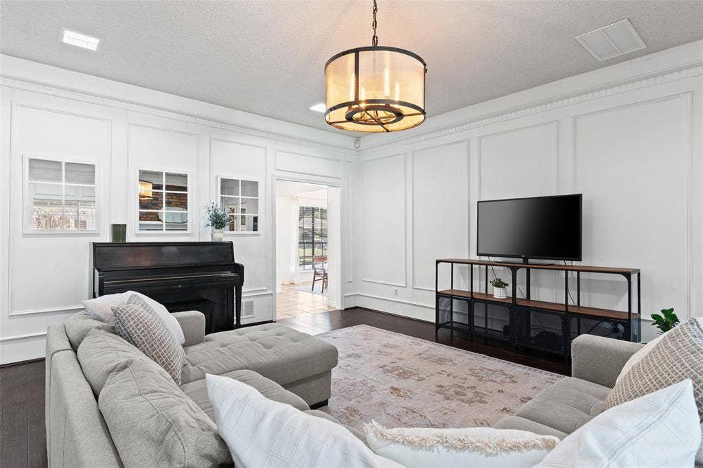 841 Villa Ridge Drive, Garland, TX 75043 Sophisticated living room showcasing elegant architectural millwork, a pendant light fixture with brass accents, dark wood-finish flooring, and a built-in media console with open shelving