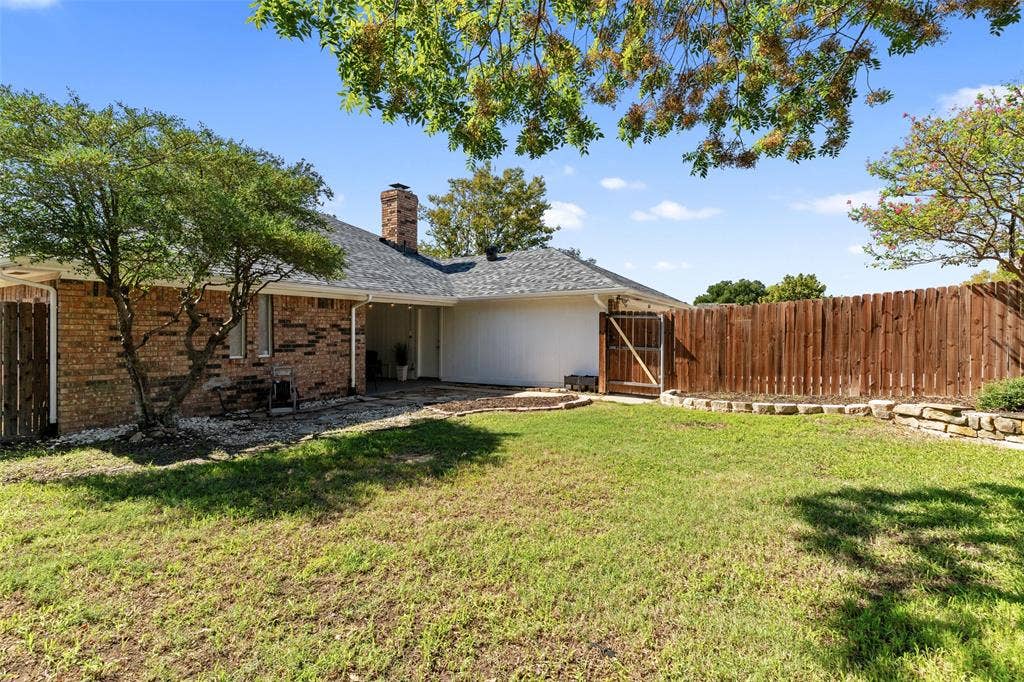841 Villa Ridge Drive, Garland, TX 75043 Expansive backyard with a manicured lawn, wood privacy fence, and stone retaining wall
