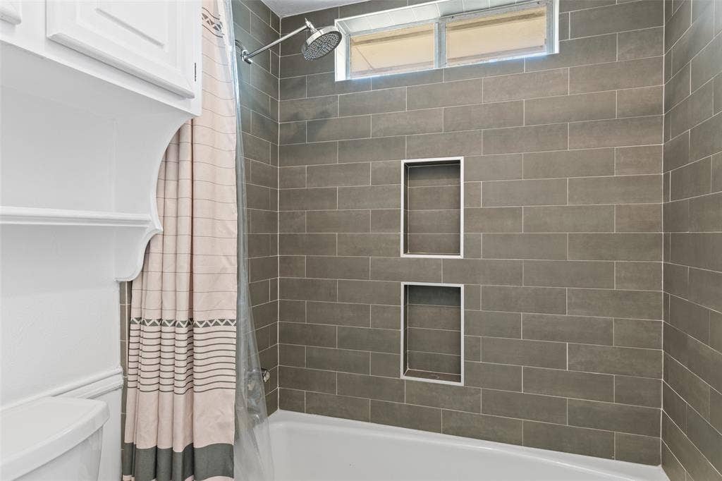 841 Villa Ridge Drive, Garland, TX 75043 Bathtub with subway tile surround, rain shower head, dual recessed shower niches, and an overhead transom window