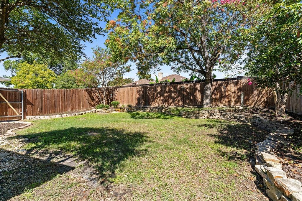 841 Villa Ridge Drive, Garland, TX 75043 Expansive yard featuring a wood privacy fence, stone retaining walls, mature trees, and a wooden gate