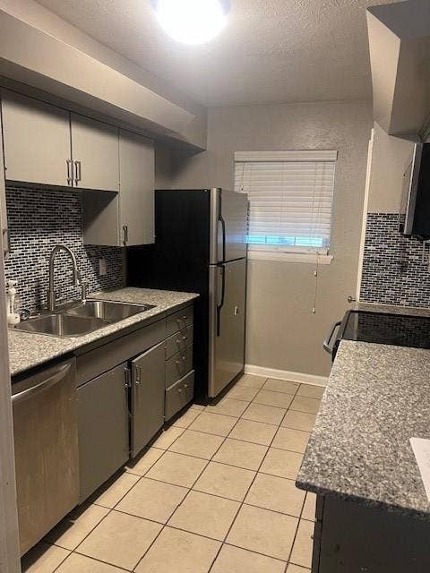Kitchen featuring stainless steel appliances, dual basin sink, light-colored tile flooring, and speckled stone countertops
