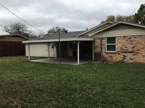 Expansive grassy area with a brick exterior, covered patio, and a separate storage structure