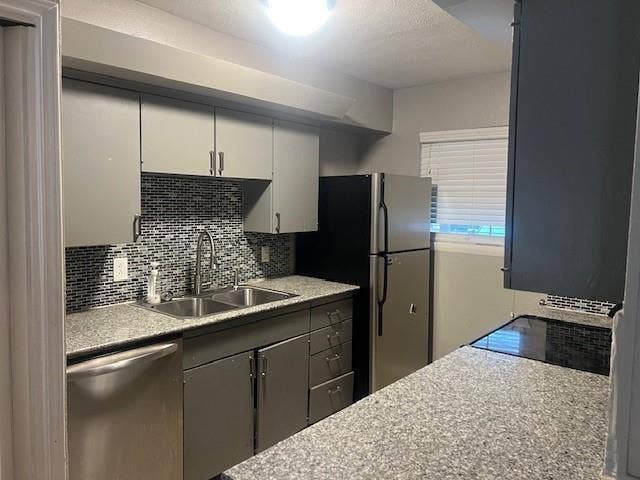 Kitchen featuring gray cabinetry, a mosaic tile backsplash, a double basin stainless steel sink, and stainless steel appliances