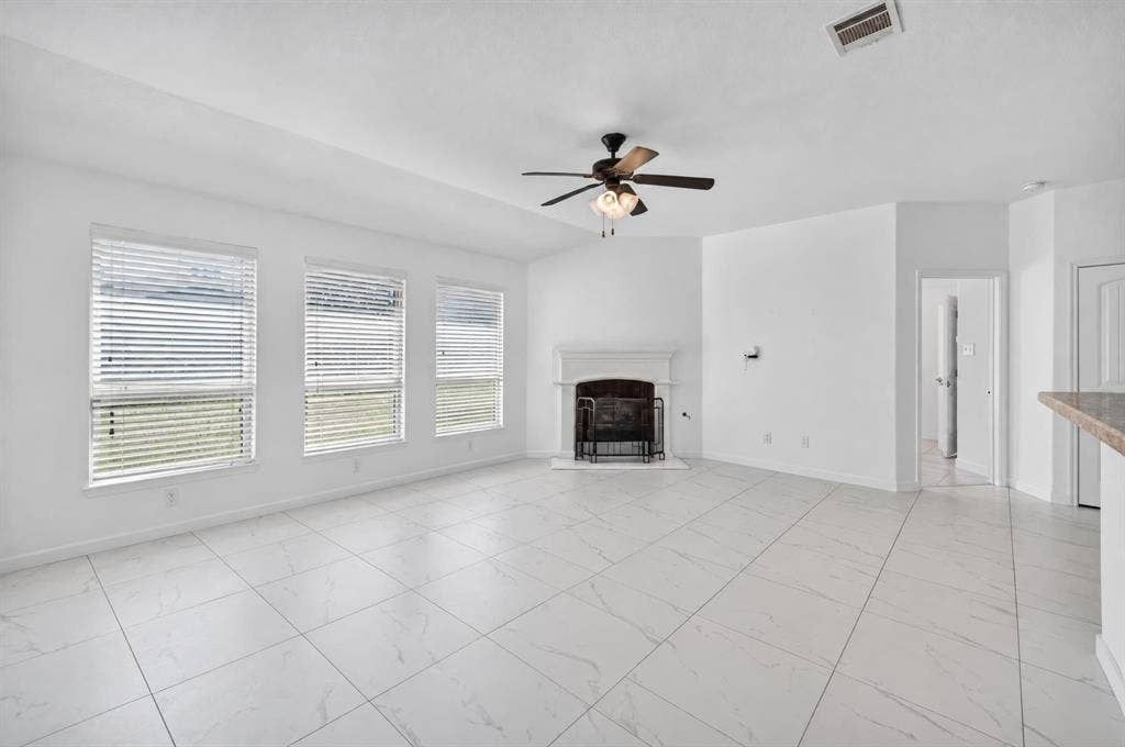 1048 Mercury Drive, Lavon, TX 75166 Spacious living area featuring white tile flooring, a fireplace with a white mantel, three large windows, a ceiling fan, and vaulted ceilings