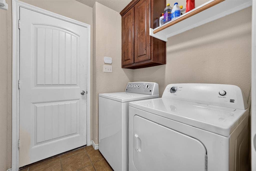 1048 Mercury Drive, Lavon, TX 75166 Laundry area featuring overhead wood-finish cabinetry, a wall-mounted shelving unit, and tile flooring