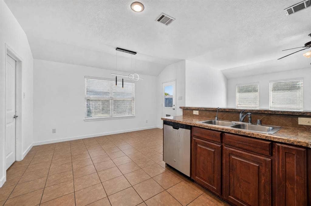 1048 Mercury Drive, Lavon, TX 75166 Open-concept living space with tile flooring throughout, featuring a kitchen island with a double basin sink and stainless steel dishwasher, and a dining area with a modern pendant light fixture