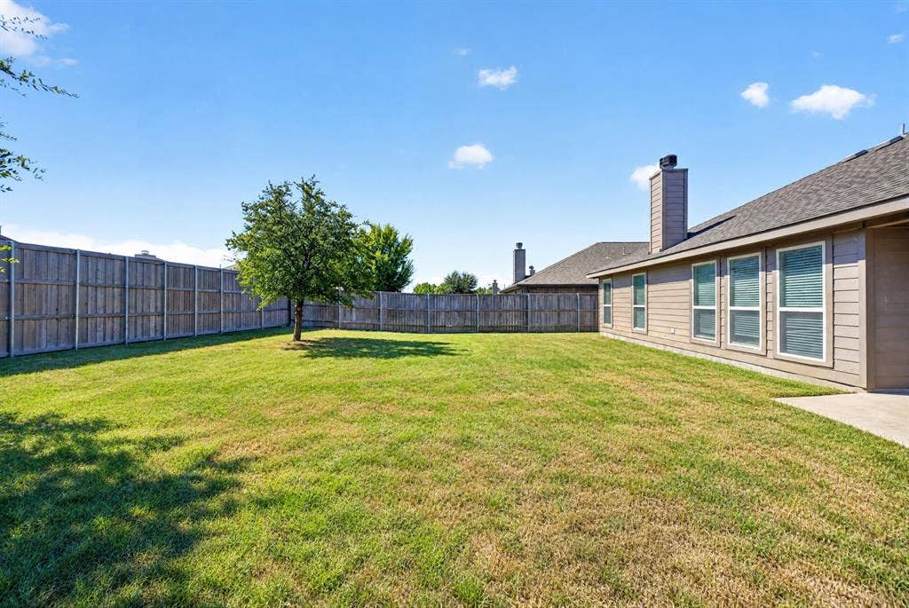 1048 Mercury Drive, Lavon, TX 75166 Expansive backyard featuring a natural wood privacy fence, mature tree, and a concrete patio