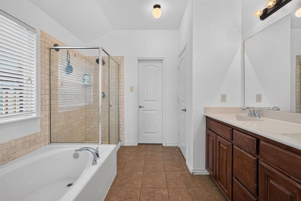 1048 Mercury Drive, Lavon, TX 75166 Enclosed glass shower with tiled surround, soaking tub, dual vanity with wood-finish cabinetry, and tiled flooring