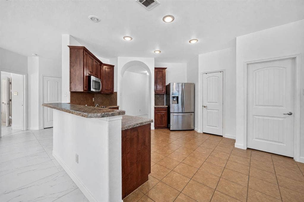 1048 Mercury Drive, Lavon, TX 75166 Kitchen featuring wood-finish cabinetry, stainless steel appliances, a breakfast bar with stone-look countertop, recessed lighting, and tile flooring