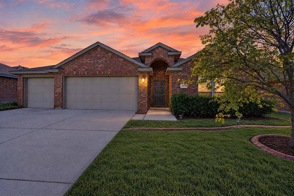 1048 Mercury Drive, Lavon, TX 75166 Brick exterior with a gabled roofline, two-car garage with panel doors, concrete driveway, and established front landscaping