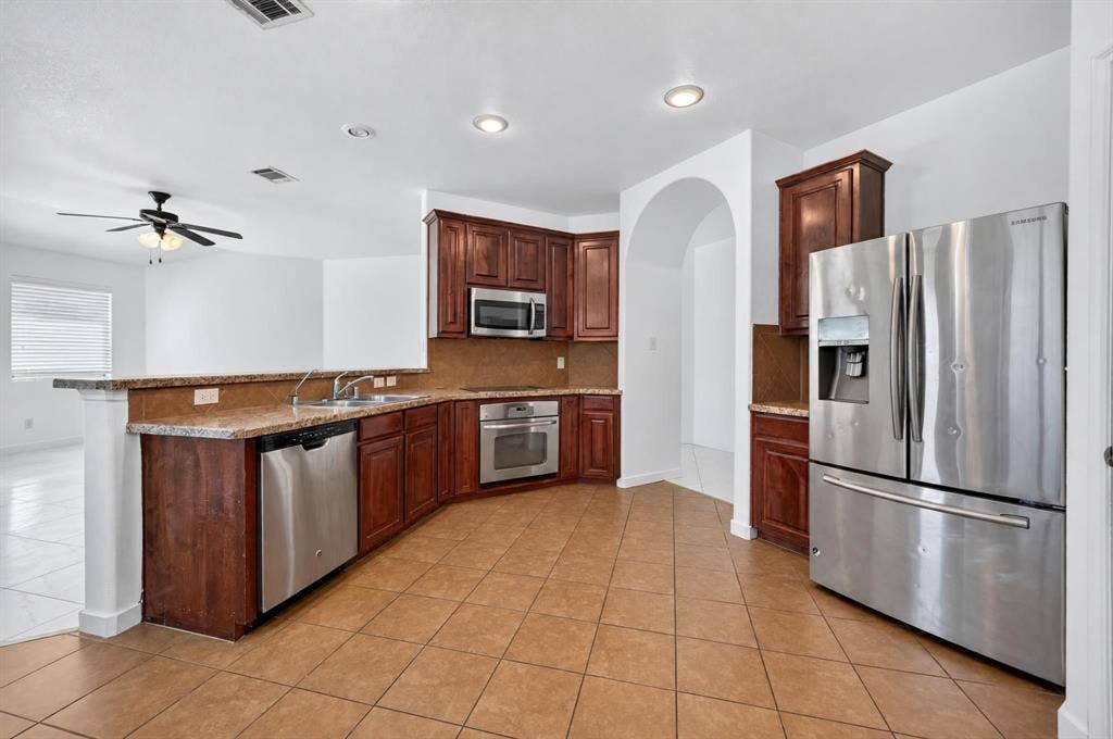 1048 Mercury Drive, Lavon, TX 75166 Kitchen featuring stainless steel appliances, wood-finish cabinetry, tile flooring, recessed lighting, and an arched doorway