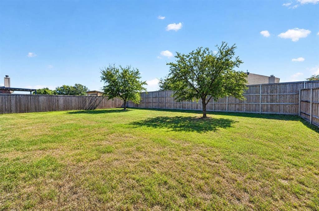 1048 Mercury Drive, Lavon, TX 75166 Expansive backyard featuring a natural grass lawn, full privacy fencing, and mature trees providing natural shade
