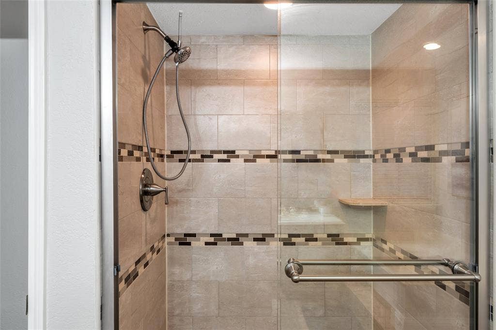4523 Wescott Drive, Grand Prairie, TX 75052 Tiled shower enclosure featuring a mosaic accent band, brushed nickel fixtures, glass shower door, and an integrated corner bench
