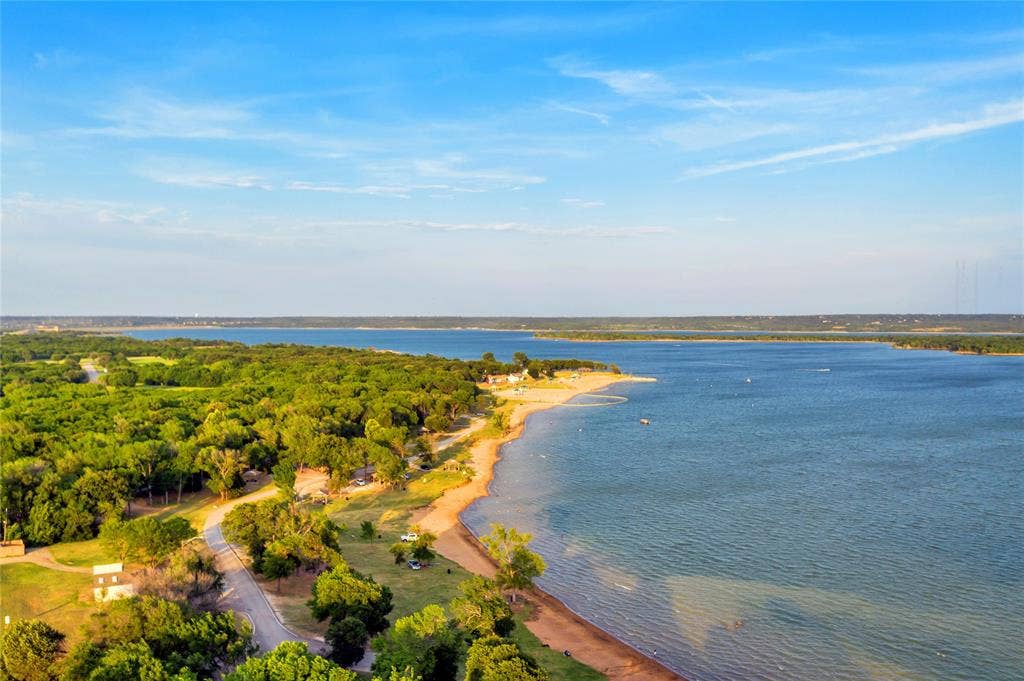 4523 Wescott Drive, Grand Prairie, TX 75052 Expansive waterfront setting with a sandy shoreline, mature trees, and a clear blue sky