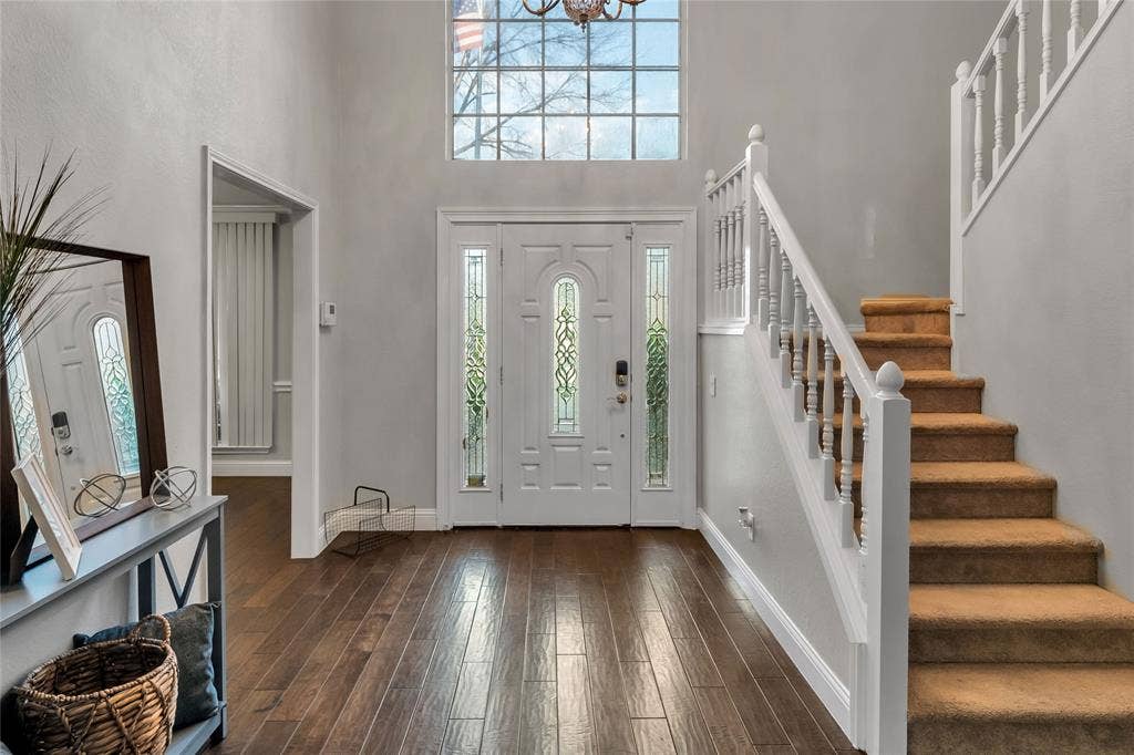 4523 Wescott Drive, Grand Prairie, TX 75052 Bright two-story foyer featuring a transom window, hardwood flooring, white-painted staircase with wooden treads, and a glass-paneled front door with sidelights