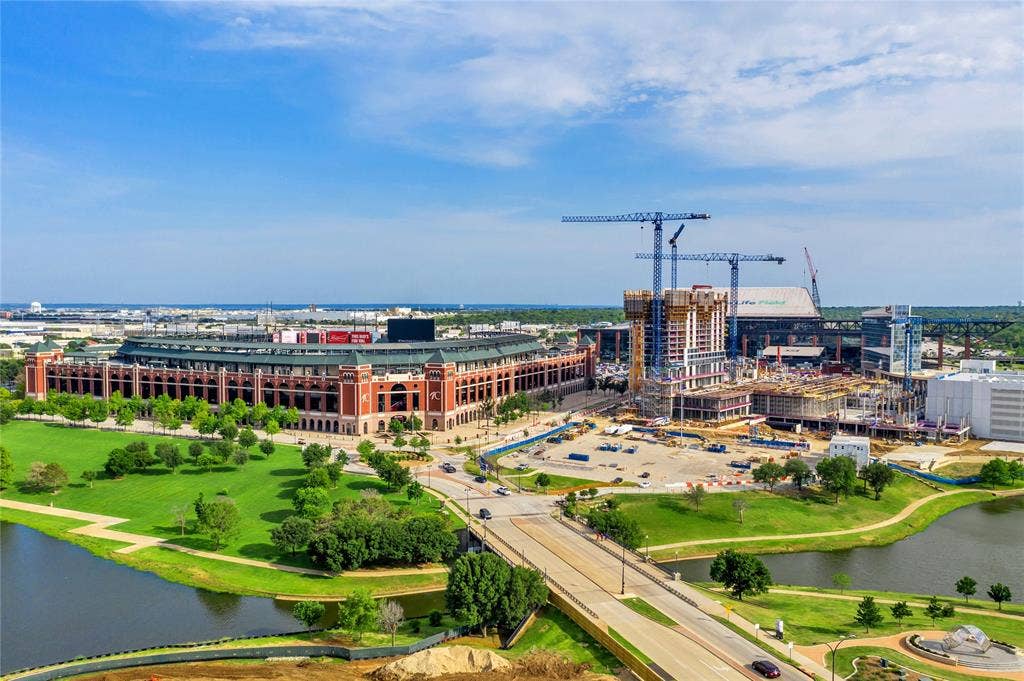 4523 Wescott Drive, Grand Prairie, TX 75052 Aerial perspective showcasing a large stadium building, surrounding green spaces, a body of water, and active construction sites with multiple cranes