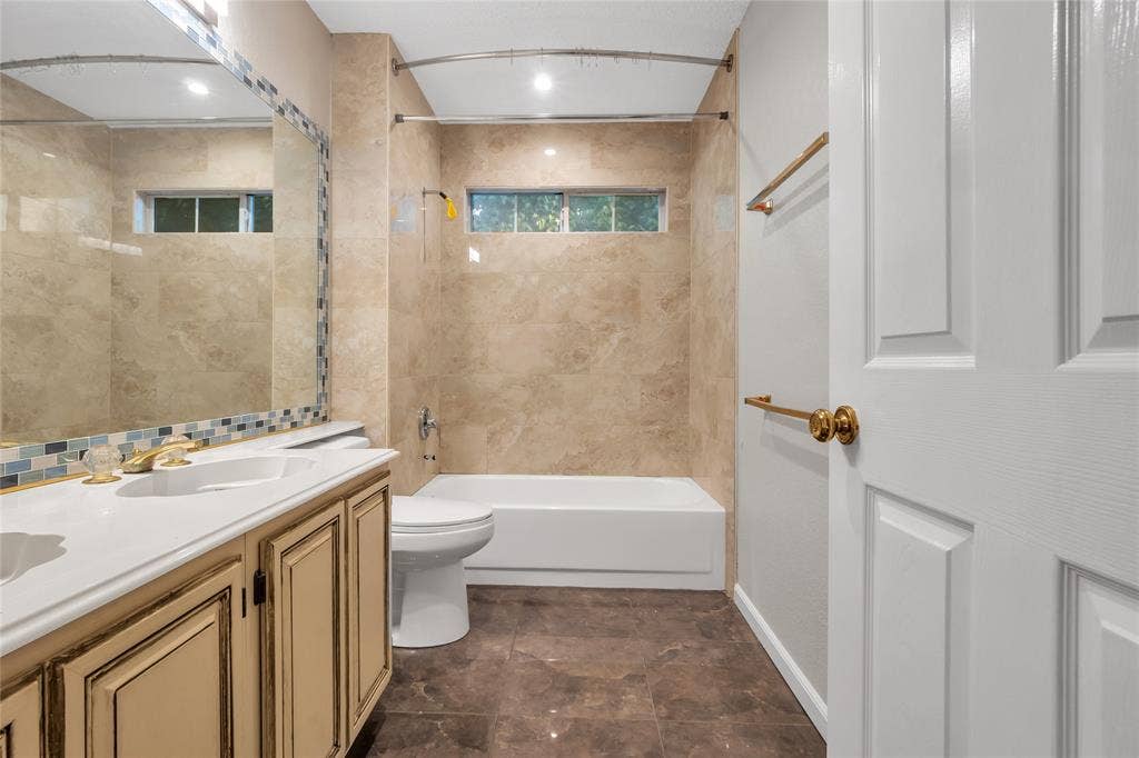 4523 Wescott Drive, Grand Prairie, TX 75052 Bathroom featuring a single vanity with an integrated sink, a rectangular mirror with mosaic tile trim, a tub/shower combination with tile surround, and brown-toned tile flooring