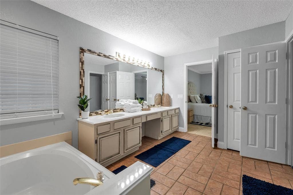 4523 Wescott Drive, Grand Prairie, TX 75052 Dual vanity with integrated sinks, large framed mirror, built-in cabinetry, and a soaking tub with brass fixtures