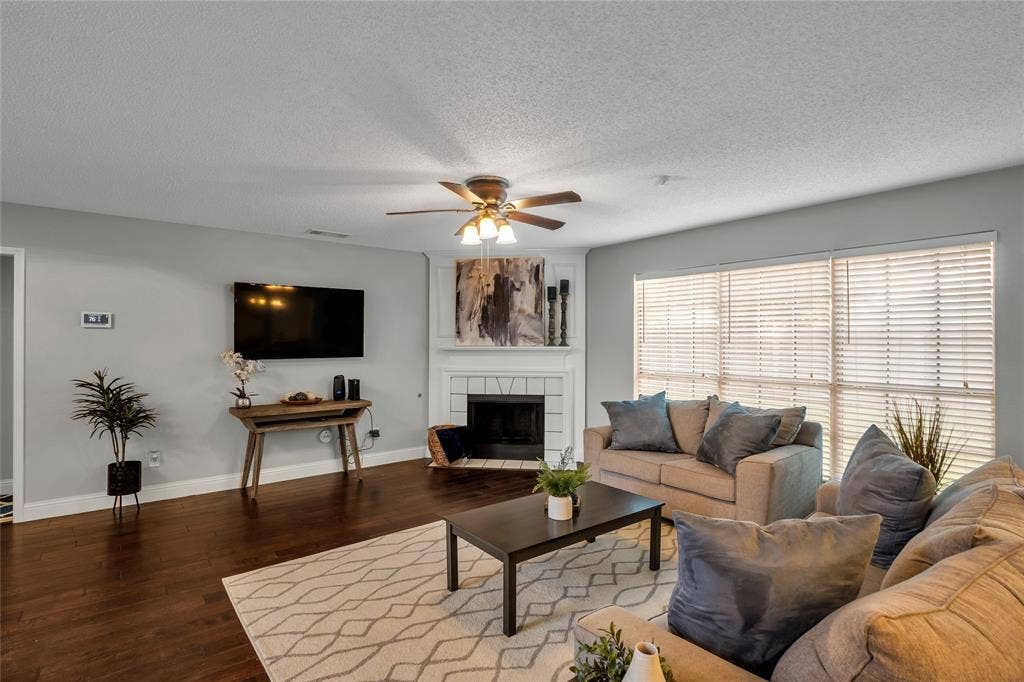 4523 Wescott Drive, Grand Prairie, TX 75052 Hardwood flooring, fireplace with white mantel, ceiling fan with integrated lighting, multiple windows with blinds, and light-toned walls