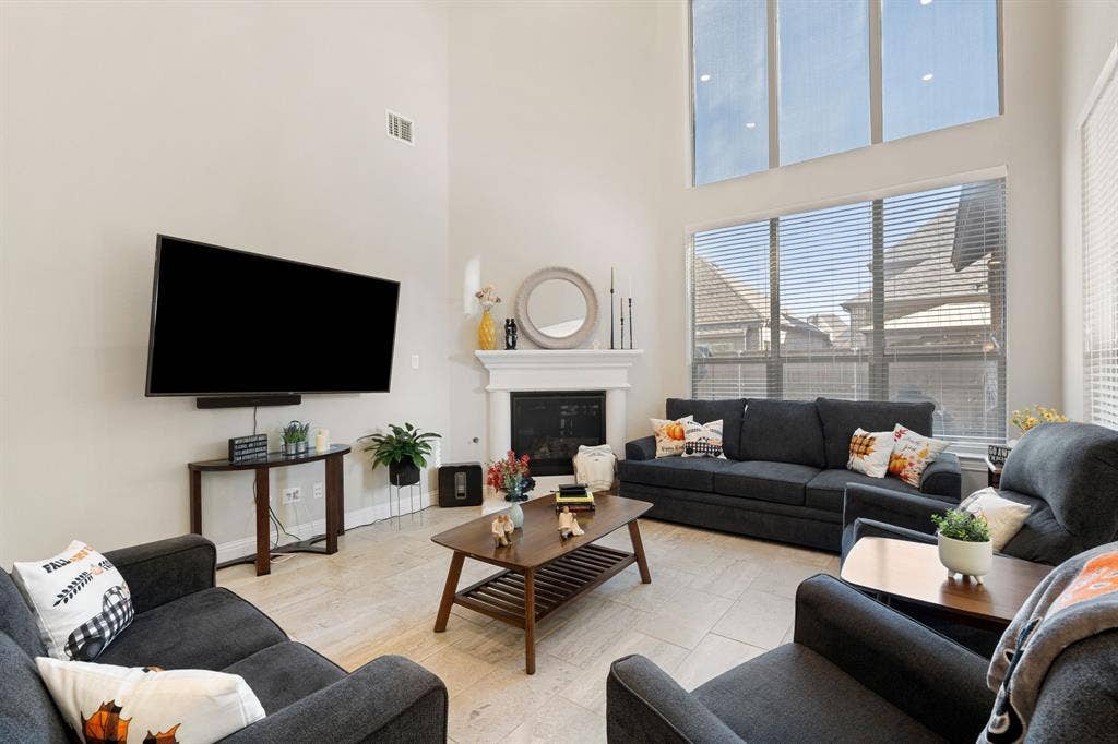 Living area featuring a floor-to-ceiling fireplace with a white mantel, expansive windows, high ceilings, and tiled flooring