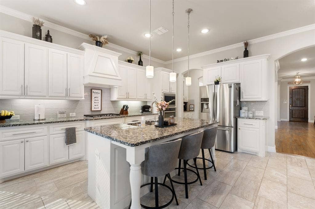 White cabinetry with crown molding, stone countertops, stainless steel appliances, tile flooring, and a central island with pendant lighting