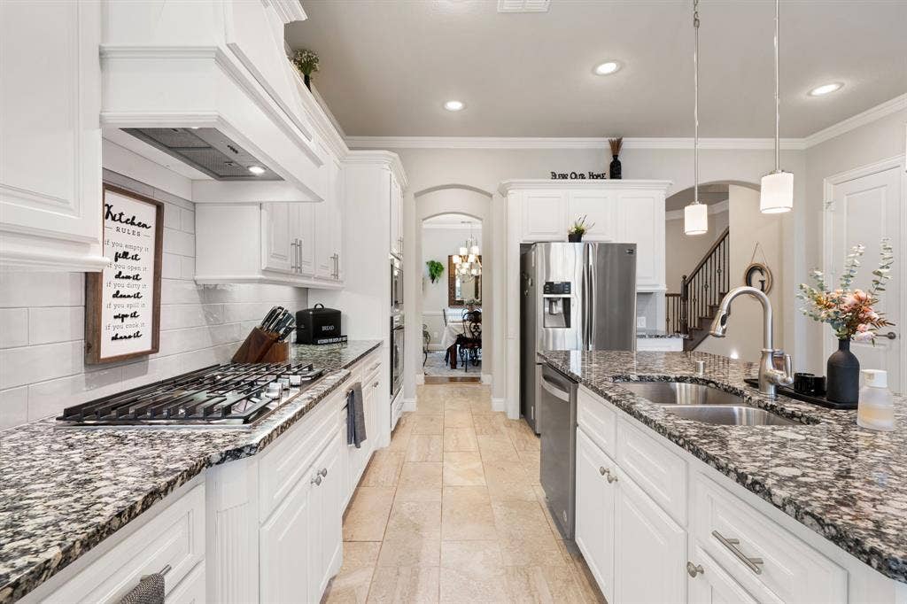 Gourmet kitchen featuring white cabinetry, granite countertops, stainless steel appliances, a gas cooktop, and a double basin sink with a gooseneck faucet